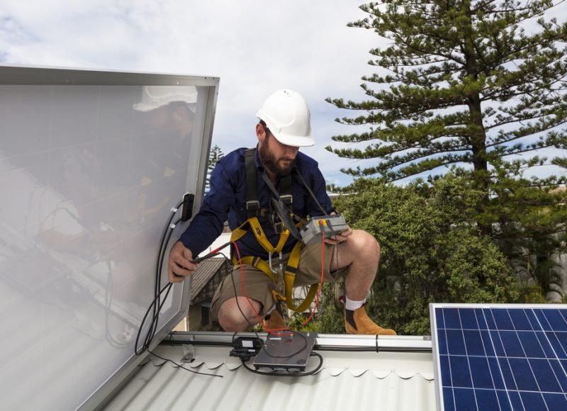 Solar panel technician measuring solar output on roof